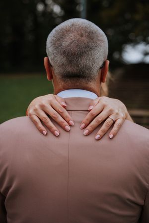 Woman placing hands on mans shoulders from behind at outdoor wedding.