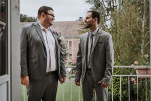 Two people in grey suits having a conversation on a balcony.