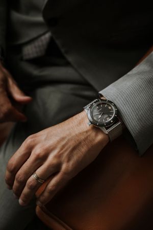 Close-up of a silver watch and wedding ring on a suited arm.