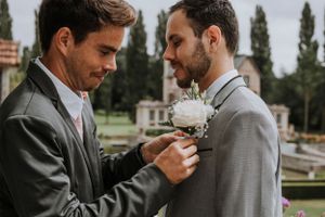 Two people in grey suits sharing an intimate moment while adjusting boutonnieres.