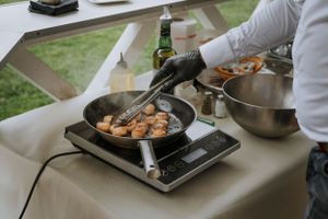 Food being prepared on portable cooking stations at an outdoor event.