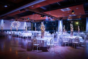 Elegant wedding reception hall with round tables, tall floral centerpieces, and romantic purple uplighting.