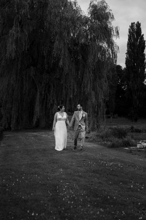 A black and white wedding photo captured under weeping willow trees in a park setting.