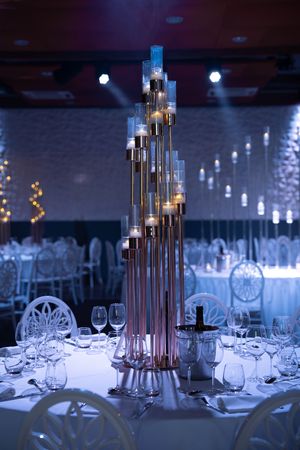 Elegant wedding reception table with tall candelabra centerpiece under blue ambient lighting.