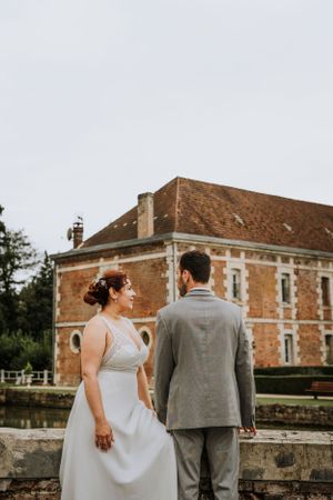 A couple photographed from behind against the backdrop of a historic brick mansion.