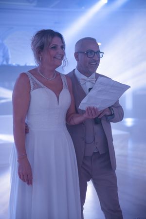 Bride and groom smiling together on dance floor reading speech at wedding reception.
