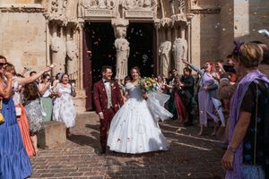 Bride and groom exit ornate church doors as guests celebrate with confetti at an elegant outdoor wedding ceremony.