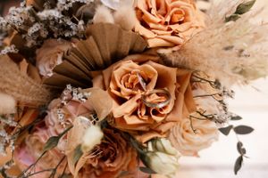 Close-up detail of peachy-orange roses and dried floral elements in soft lighting.