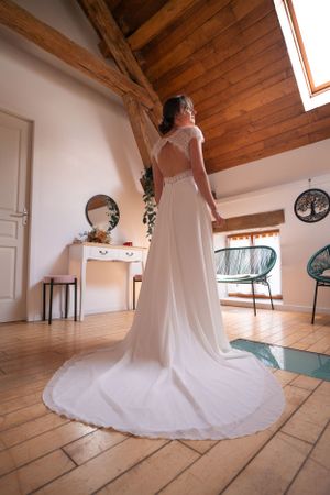 A flowing white wedding dress with train displayed on rustic wooden flooring in an attic space.