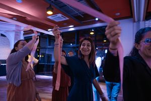 A smiling woman in a blue dress dances joyfully with guests at a wedding reception party.