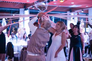 Bride in white dress and groom celebrating with balloons and streamers at wedding reception.