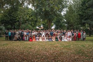 Large wedding group photo with guests gathered outdoors in a lush green park setting.
