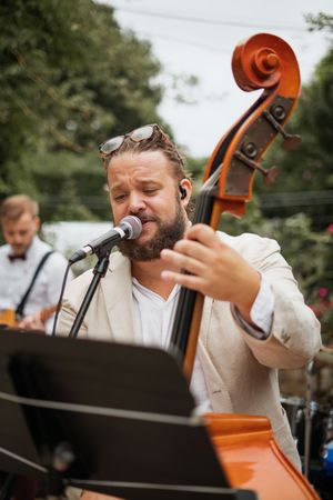 Bearded musician passionately singing and playing double bass at an outdoor wedding reception.