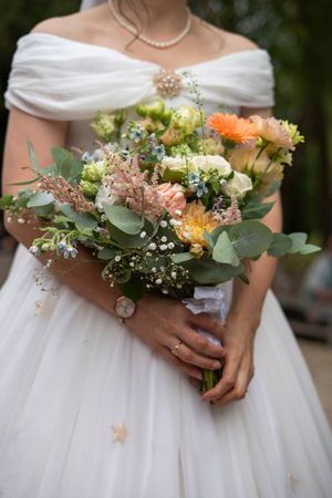 Bride in white off-shoulder gown holding a colorful bouquet of orange, pink, and white flowers.