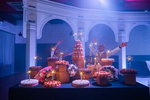 Elegant wedding dessert table with tiered cakes and sparklers in a grand blue-lit arched venue.