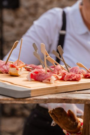 Wooden serving board with prosciutto appetizers arranged with toothpicks.