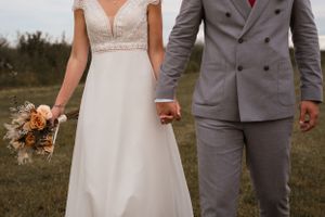 Wedding couple in grey suit and white dress standing together outdoors.