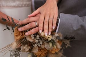 Hands holding a rustic dried flower bouquet with neutral tones and textures.