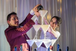 Couple pouring champagne into an elegant martini glass tower at their wedding reception.