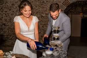 Couple pouring champagne into a tower of glasses at their wedding reception.