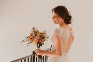 Bride in lace wedding dress holding floral bouquet in rustic interior setting.