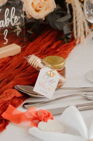 Wedding table details with place cards and coral fabric runner decorated with floral arrangements.