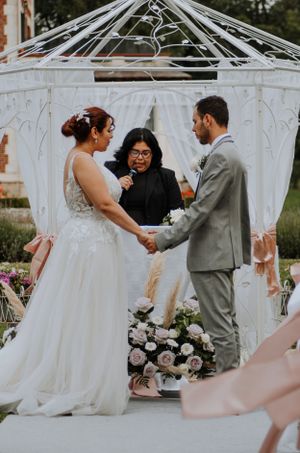 Wedding ceremony taking place under a white gazebo decorated with flowers.