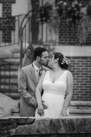 A romantic black and white wedding photo of a couple sharing a kiss on stone steps in front of a brick building.