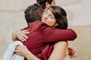Two people sharing a warm embrace at a wedding, both wearing elegant burgundy outfits.