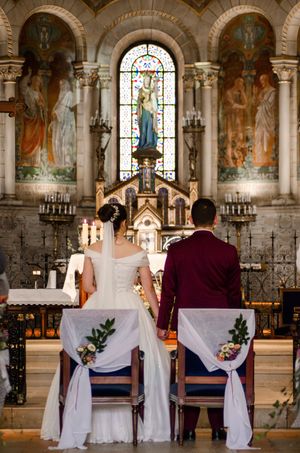 Bride and groom seated at the altar during a Catholic church wedding ceremony with stained glass windows.