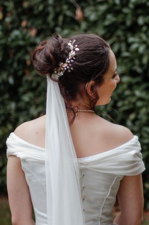 Bride with elegant updo hairstyle adorned with floral hair comb and flowing veil in white gown.