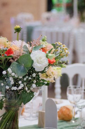 Elegant wedding table centerpiece with white, peach, and coral flowers, eucalyptus, and baby's breath in a glass vase.