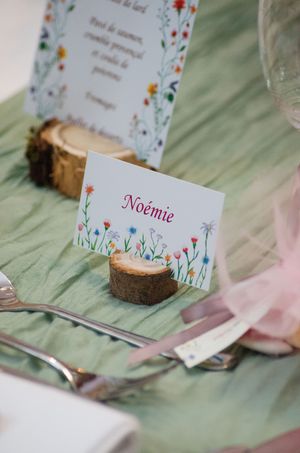 Elegant wedding place card holder made from a wood slice displaying the name Noémie with floral design.
