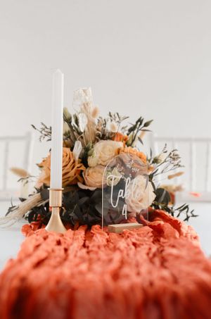 Elegant table setting with white candles and coral flowers on a textured orange runner.