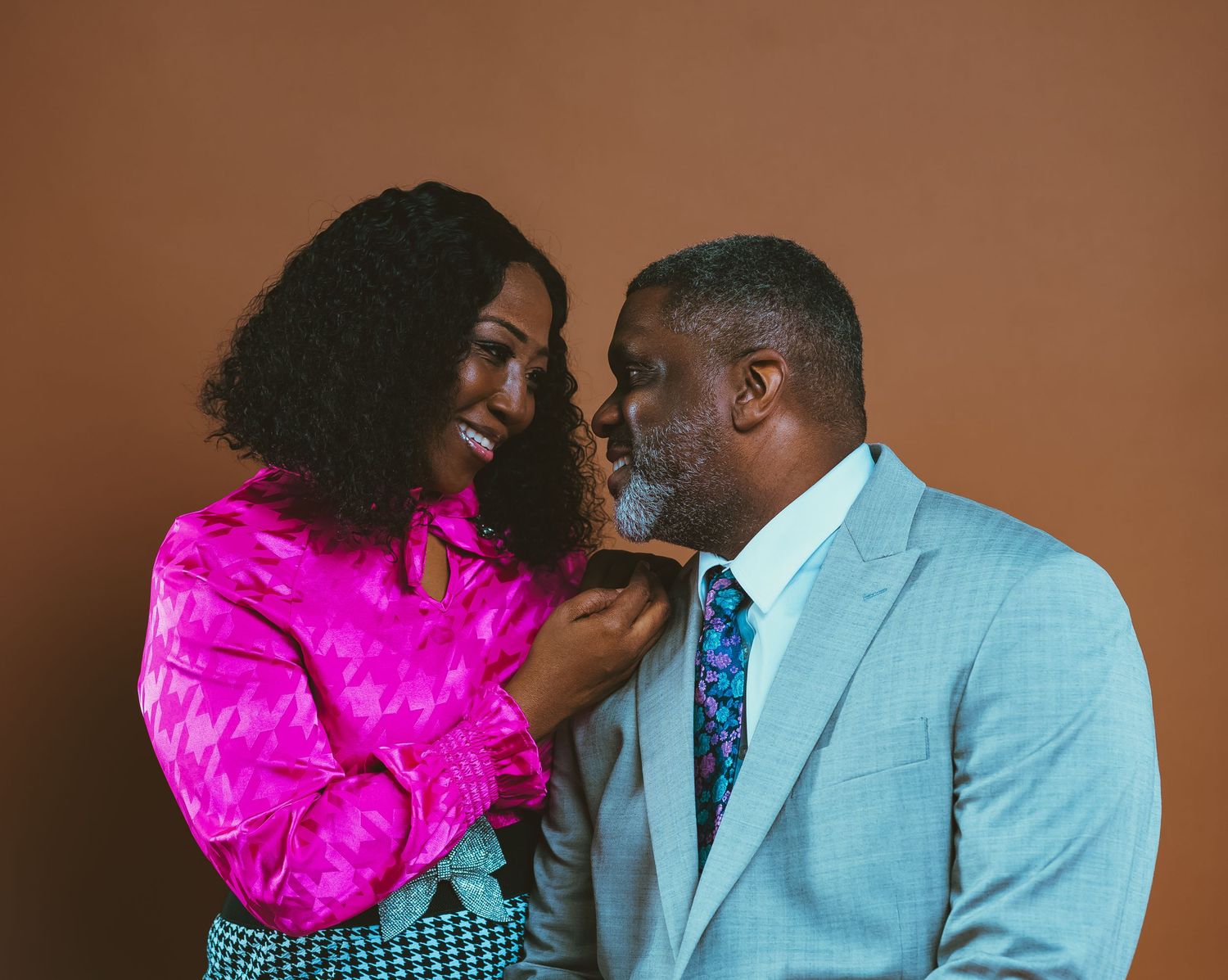 A romantic couple's portrait with one person in hot pink and another in light blue against a brown background.