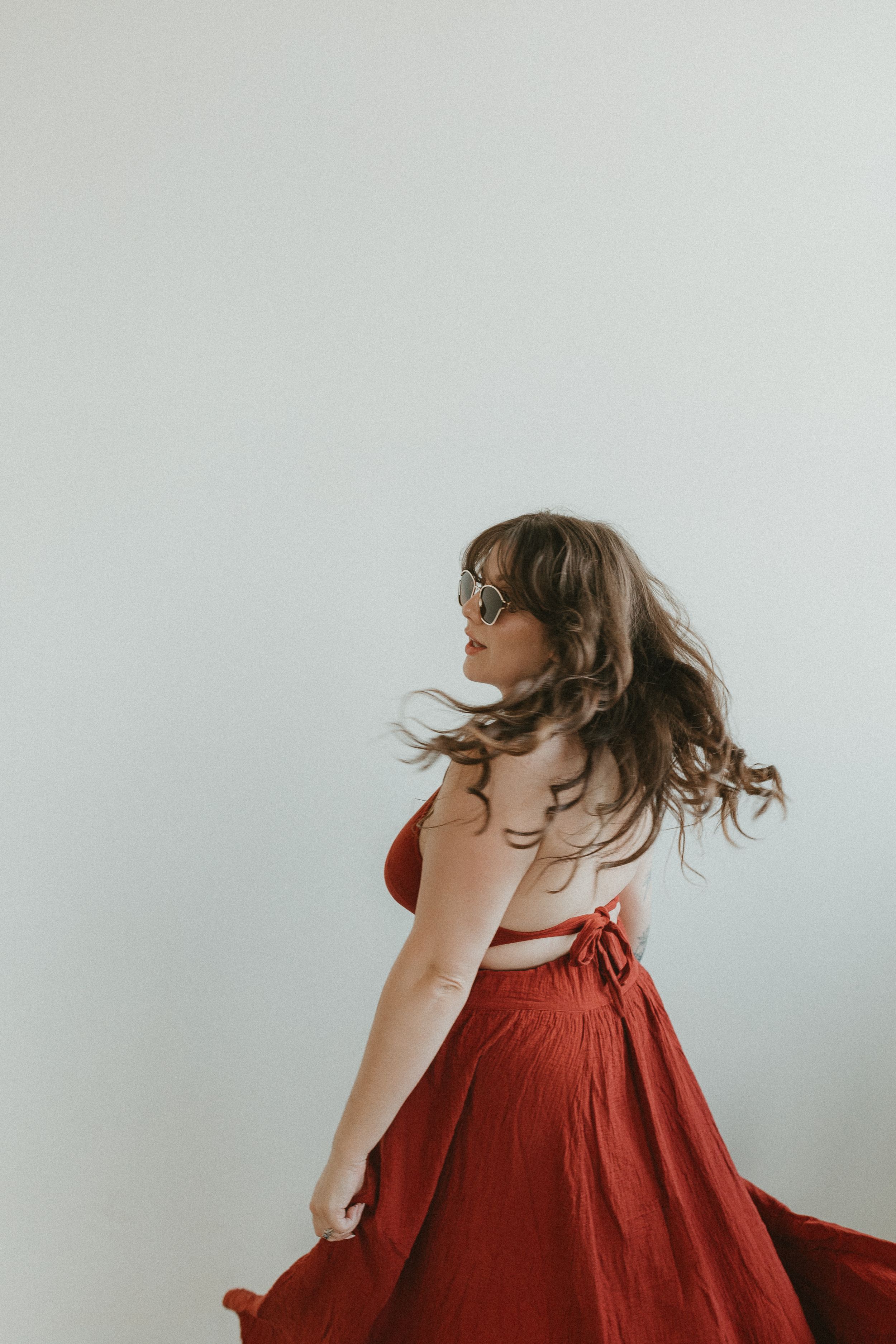 A person in a flowing red dress twirls and spins in a minimalist white studio setting, creating dynamic movement.