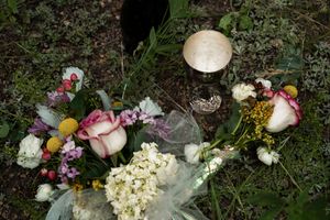 A memorial arrangement with roses, hydrangeas and assorted flowers laid on grass with a decorative stone marker.