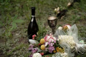A romantic outdoor picnic scene with wine, flowers, and scattered treats on the ground.