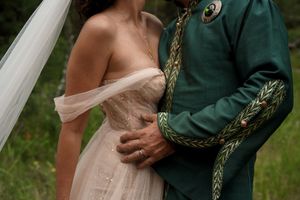 A couple embraces during a wedding ceremony, with the bride wearing blush pink and the groom in a formal green uniform.