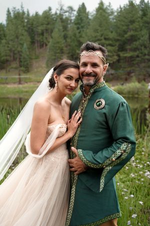 A couple in wedding attire share an intimate moment in a field of wildflowers and pine trees.