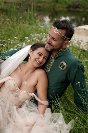 A romantic wedding couple embraces in a wildflower meadow, with the bride in blush and groom in emerald green.