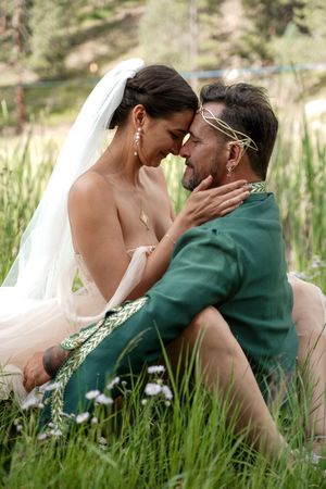 A romantic scene unfolds between newlyweds in a meadow surrounded by tall grass and nature.