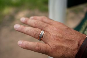 A close-up shot of a weathered hand wearing a silver wedding band on outdoor background.