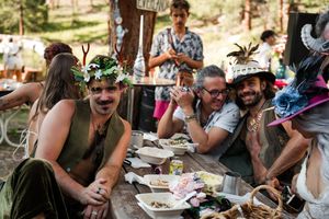 A group of festively dressed guests enjoying a meal at an outdoor table decorated for a celebration.