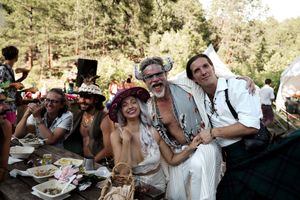 Wedding guests in bohemian attire gather at outdoor tables during a forest celebration.