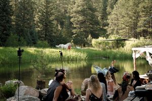 Guests watching a ceremony by a serene lake surrounded by pine trees.