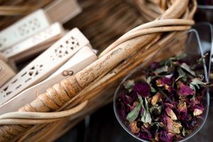 Rustic wooden utensils and dried flower petals arranged on a wooden surface.