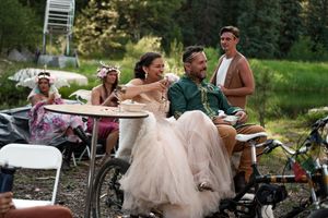 Wedding celebration guests seated at outdoor tables surrounded by forest scenery.
