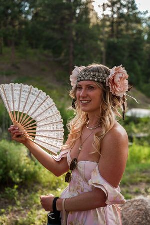 A person in pink dress holding a decorative lace fan at an outdoor event.