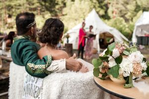A couple embraces at an outdoor wedding reception with floral decorations on a nearby table.